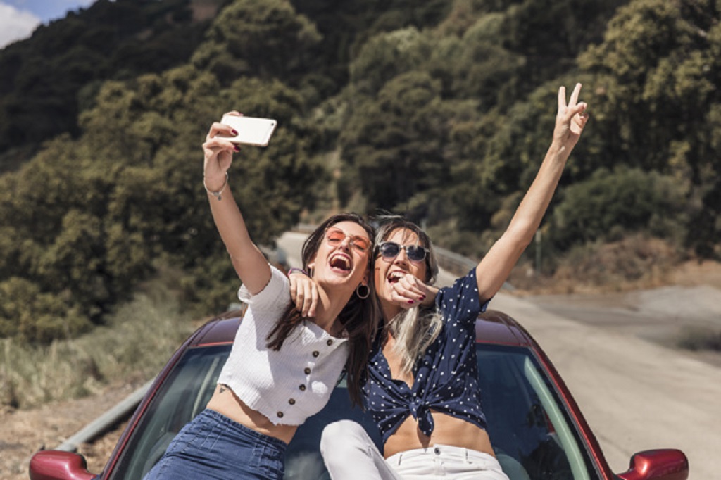 amigas-sentado-capo-coche-tomando-autorretrato_23-2147855623