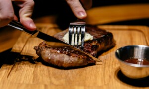 Male's hands begin to cut steak using knife and fork